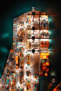 A container ship pulled up alongside a dock at night, lit up because it is night time.